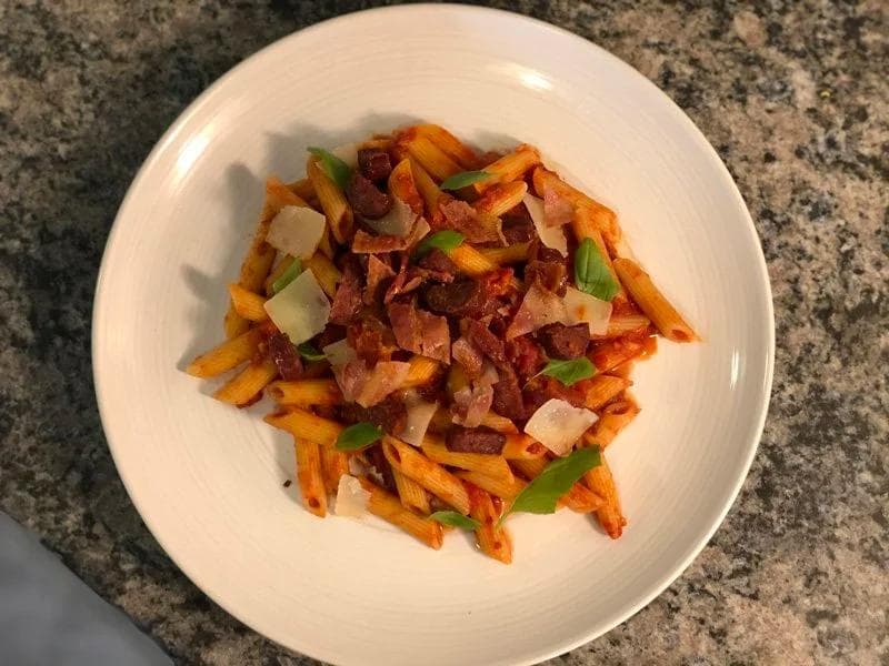 Spicy bacon and chorizo pasta with sweet potato fries, topped with crispy bacon bits, cheese, and green onions.