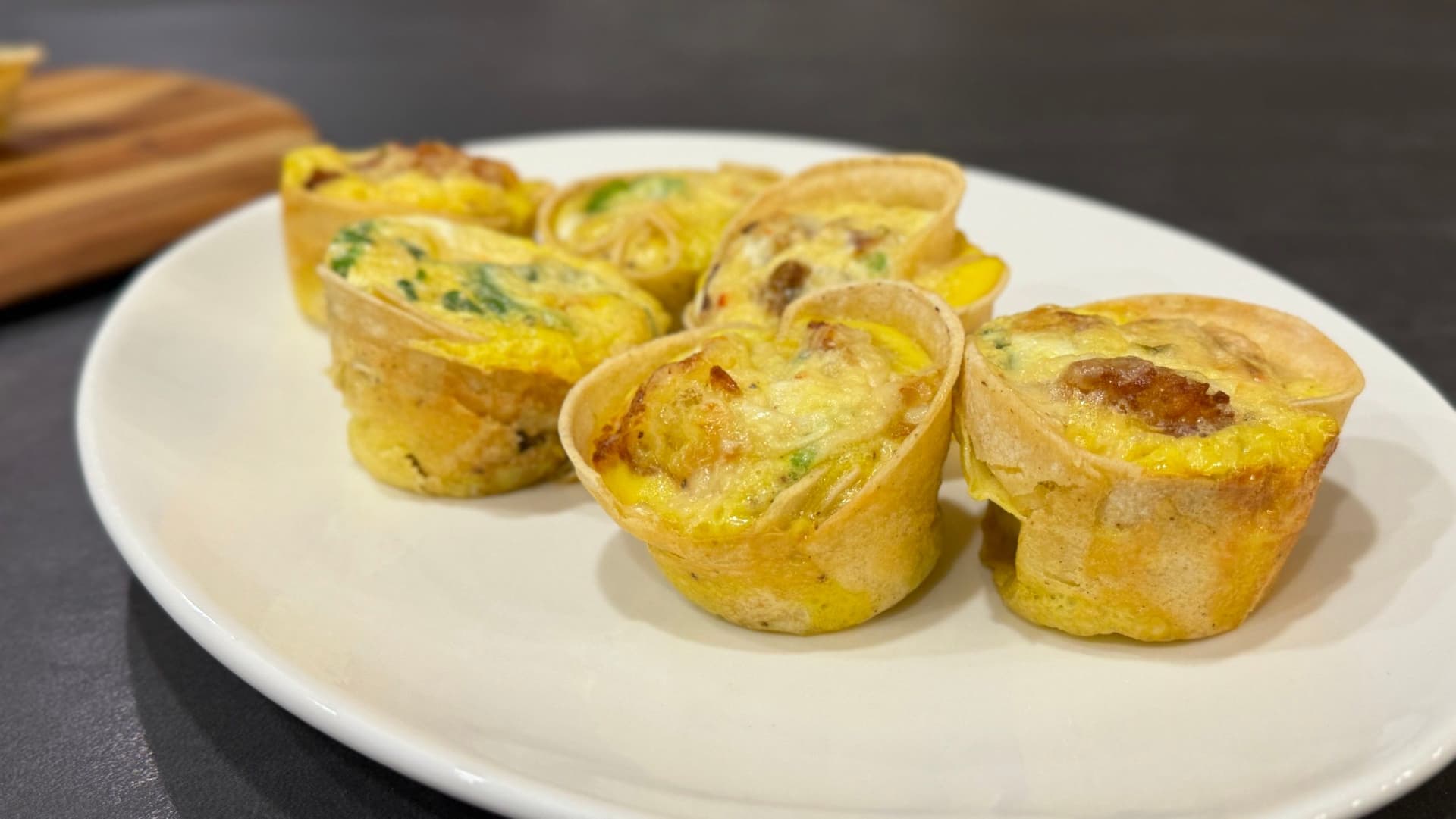 Five golden baked tortilla breakfast cups with herbs in a muffin pan, served on a white plate.