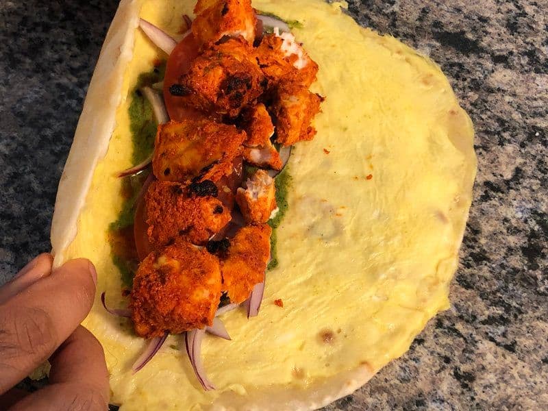 Chicken tikka pieces arranged on a yellow paratha with sliced onions before wrapping into a kathi roll.