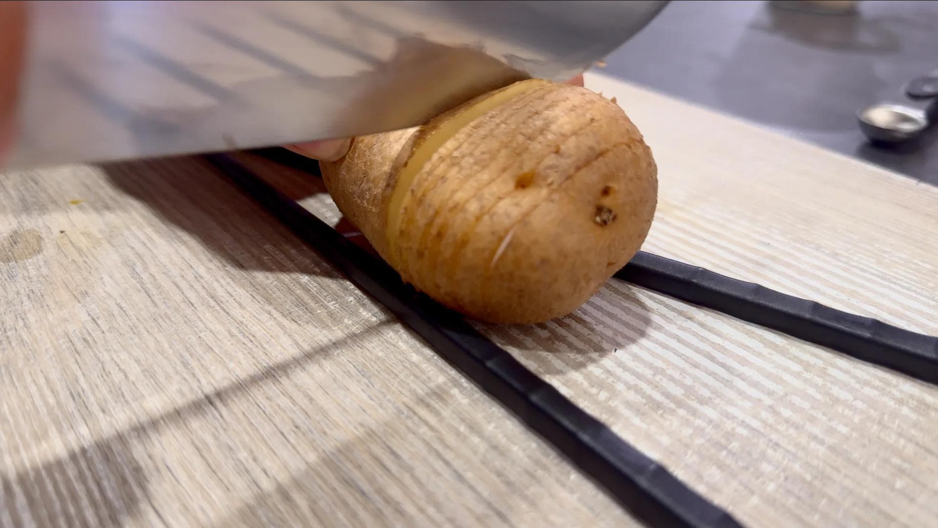 Partially sliced potato on cutting board showing thin cuts made 75% through, demonstrating hasselback slicing technique.