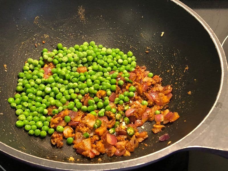 Green peas and diced potatoes with spices cooking in a wok during preparation of potato wrap filling.