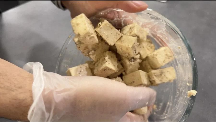 Tofu cubes coated in seasoned cornstarch mixture in a glass bowl, ready for air frying.