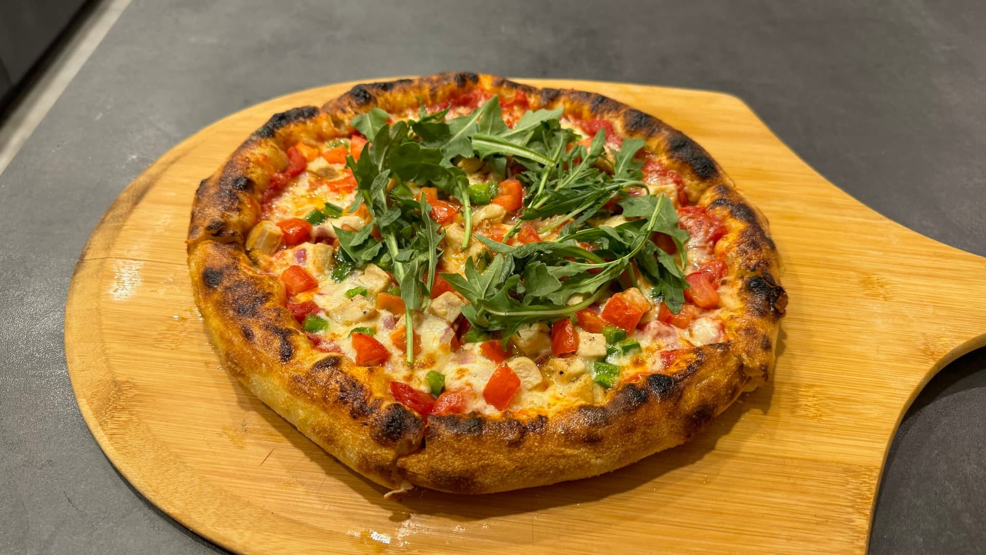 Neapolitan-style pizza topped with fresh arugula, red peppers, and cheese on a wooden serving board.