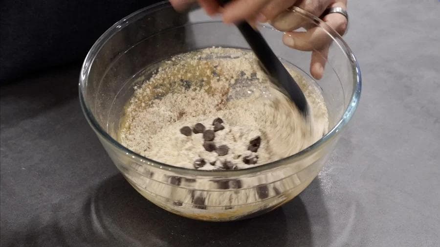 Folding chocolate chips into pumpkin cookie dough in a glass bowl with a spatula.