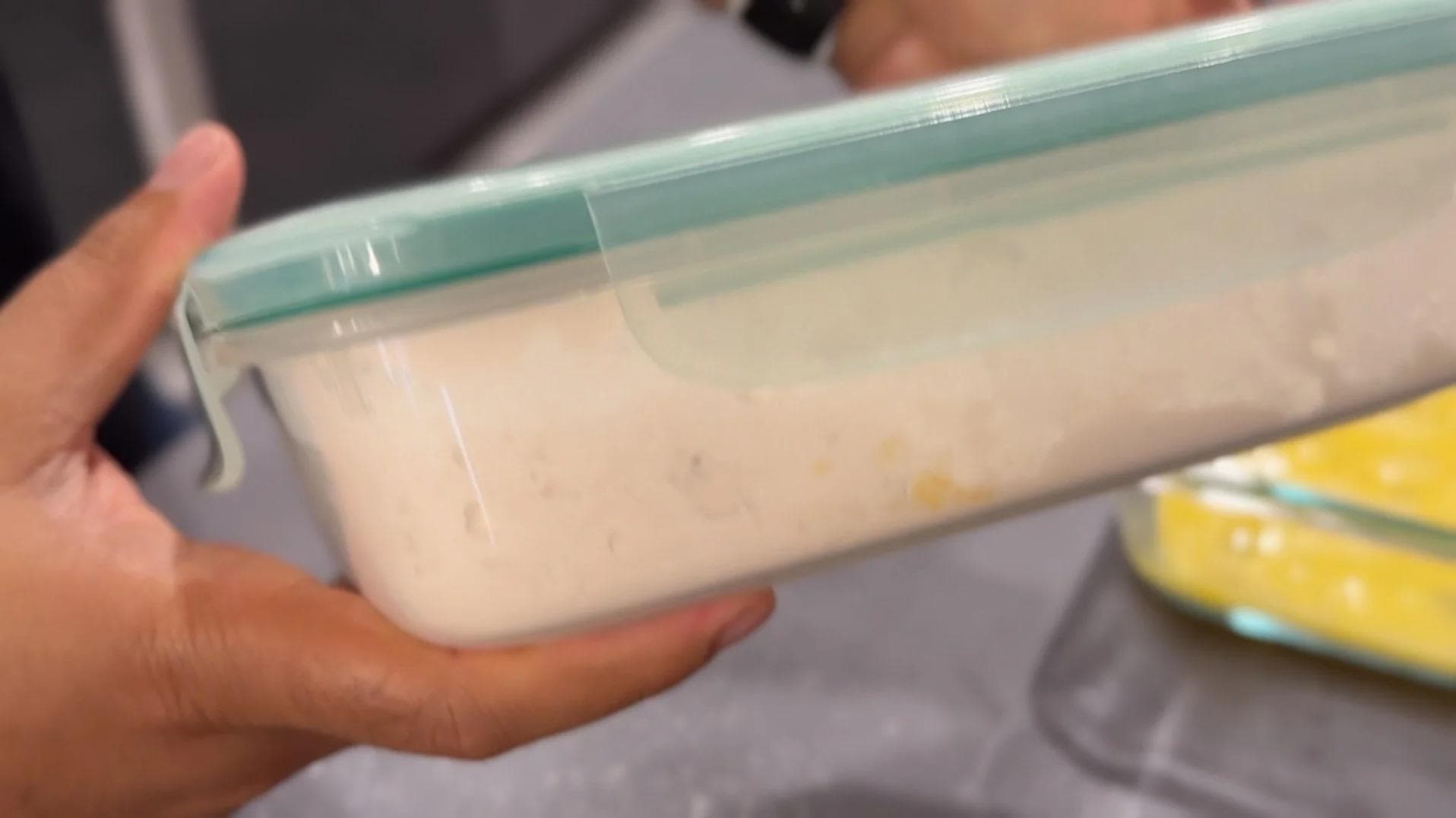 Hand holding a container of egg mixture for dipping chicken pieces in panko coating process.