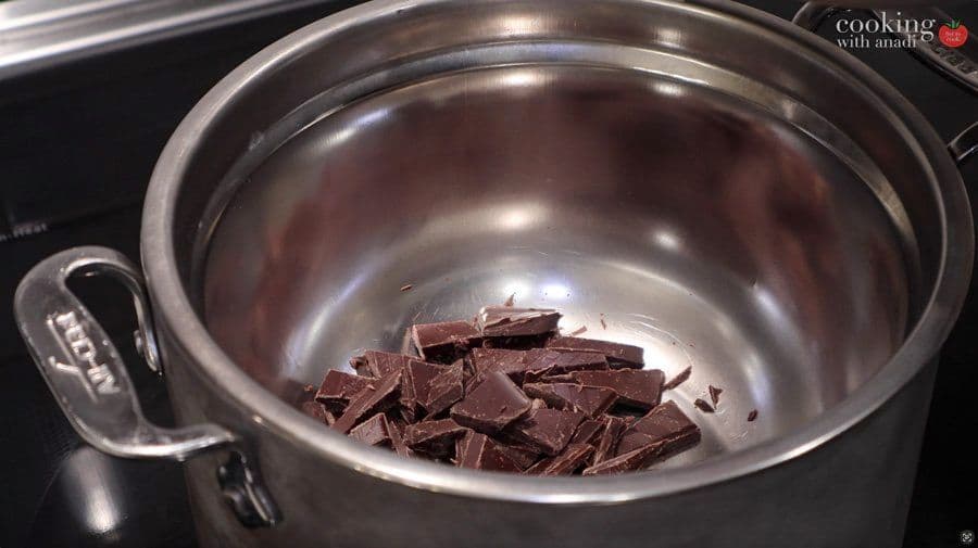 Chopped dark chocolate pieces in a stainless steel bowl over simmering water for melting.