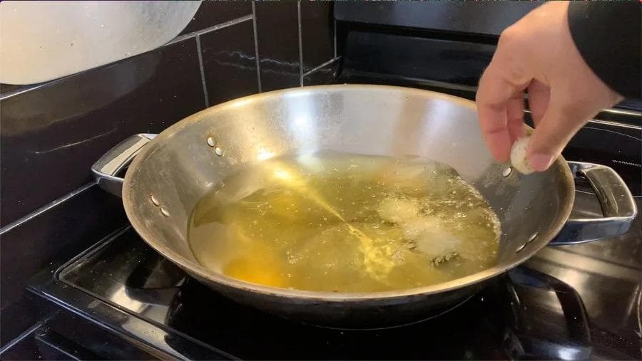 Hand adding mozzarella sticks to hot oil in a wok for frying.