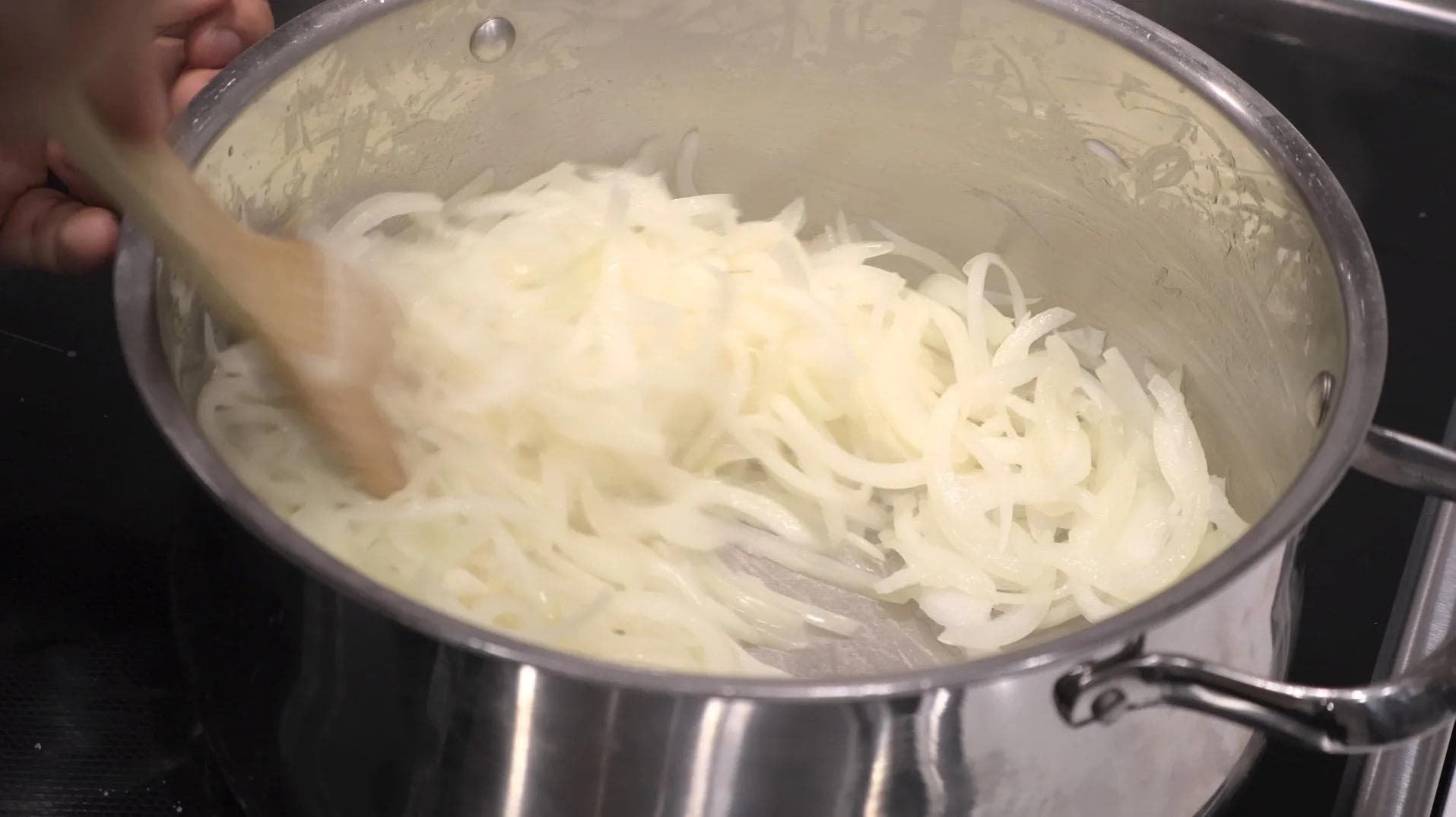 Sliced onions being stirred in a large pot with butter and oil over medium heat.