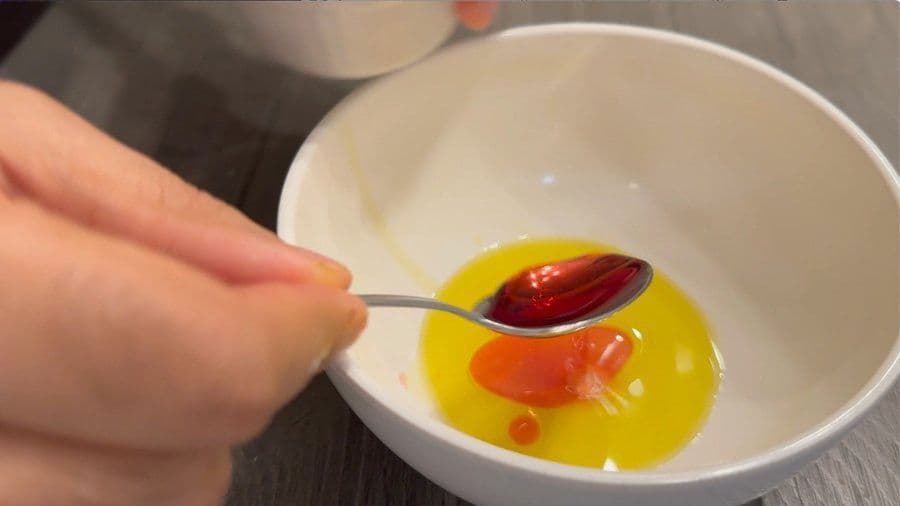 Spoon of red chimichurri sauce being held over a bowl of yellow oil and vinegar mixture.