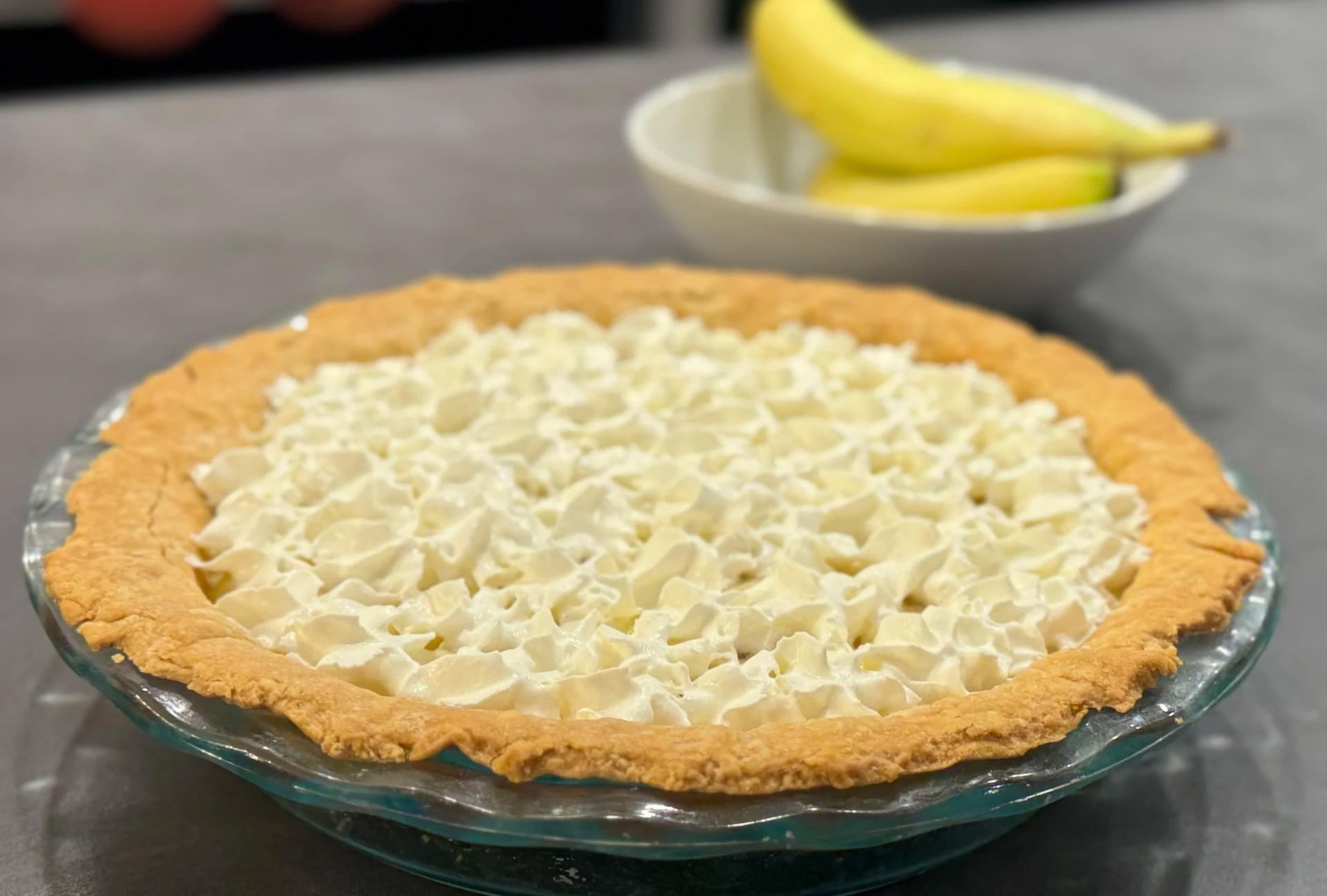 No-bake banana cream pie with graham cracker crust and whipped cream topping in glass pie dish