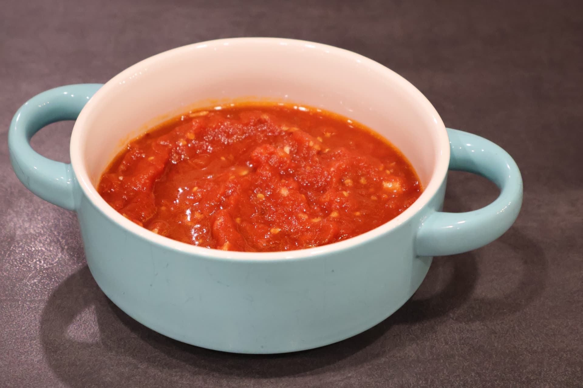 Homemade marinara sauce simmering in a light blue ceramic pot with handles