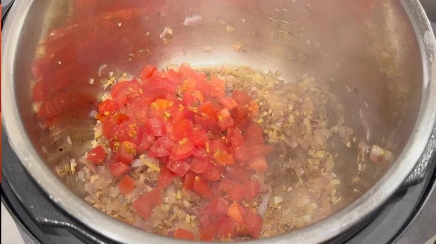 Diced tomatoes and spices cooking with ground meat and sautéed onions in an Instant Pot.