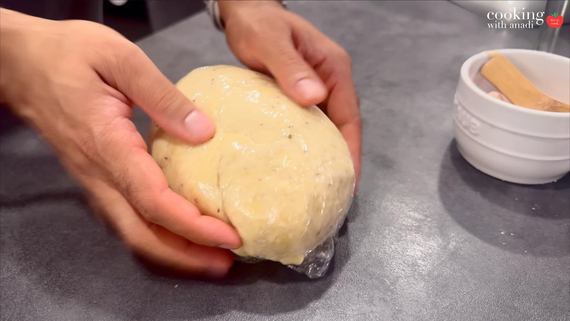 Hands holding a smooth, ball-shaped dough portion for samosa filling on a gray work surface.