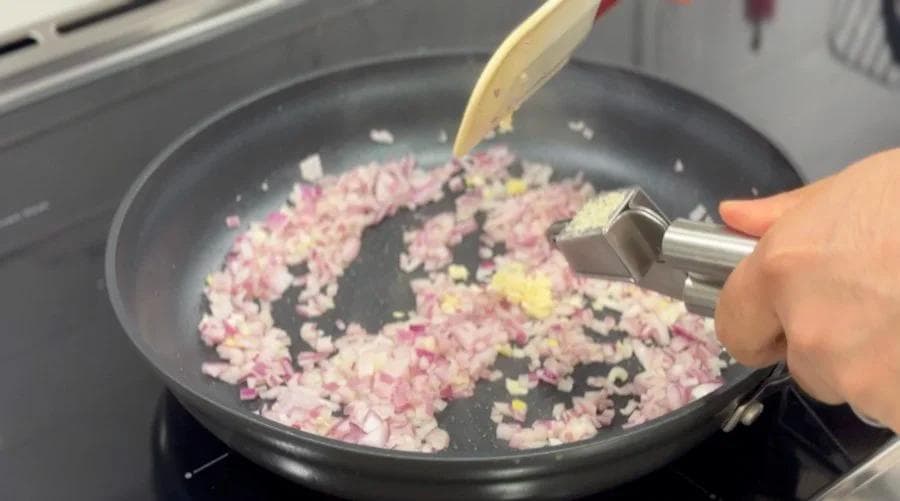 Diced pink onions and minced garlic being sautéed in olive oil in a dark skillet on stovetop.