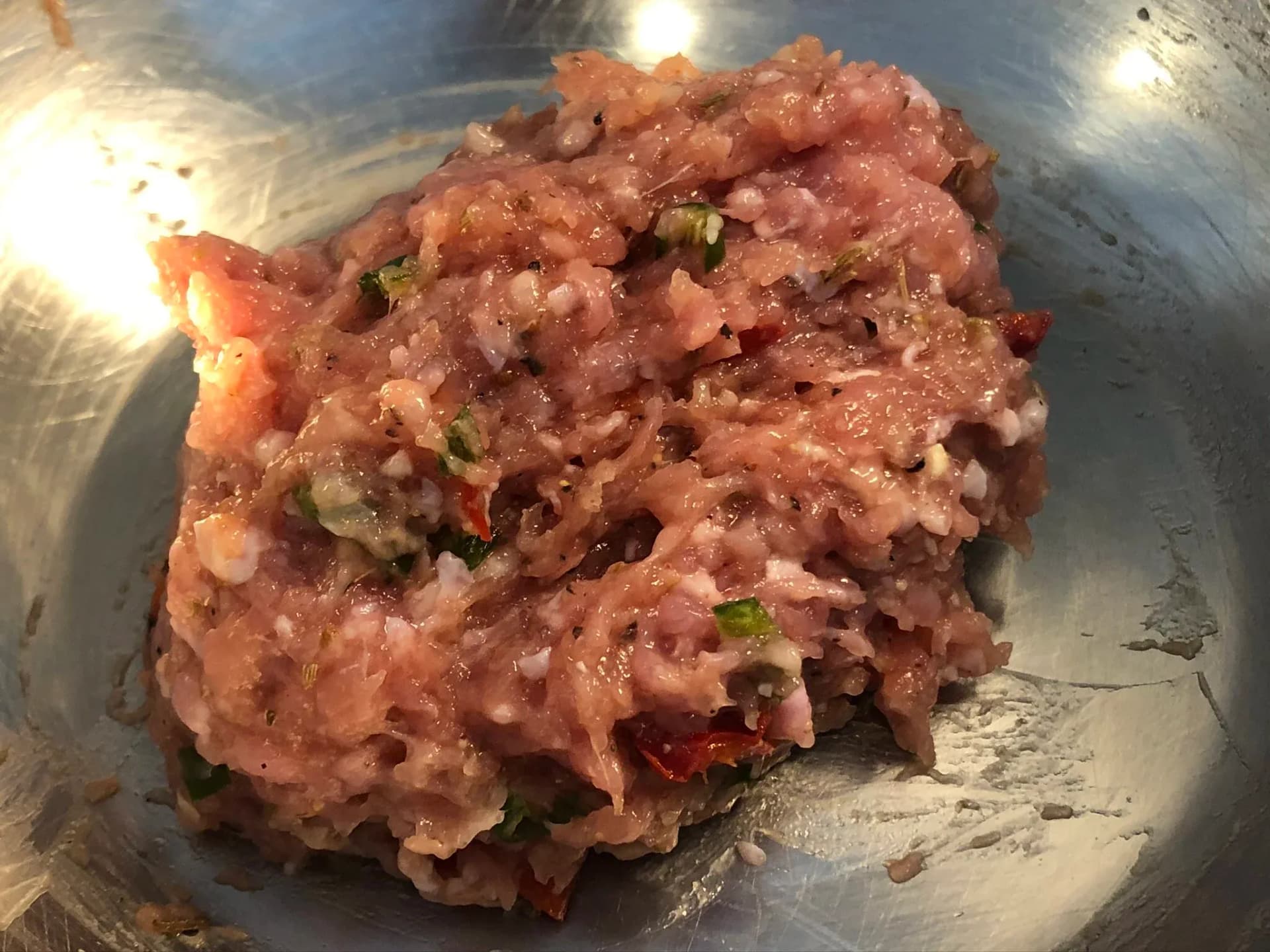 Raw spicy Italian sausage mixture with ground meat, herbs, and red chilies mixed together in a metal bowl.