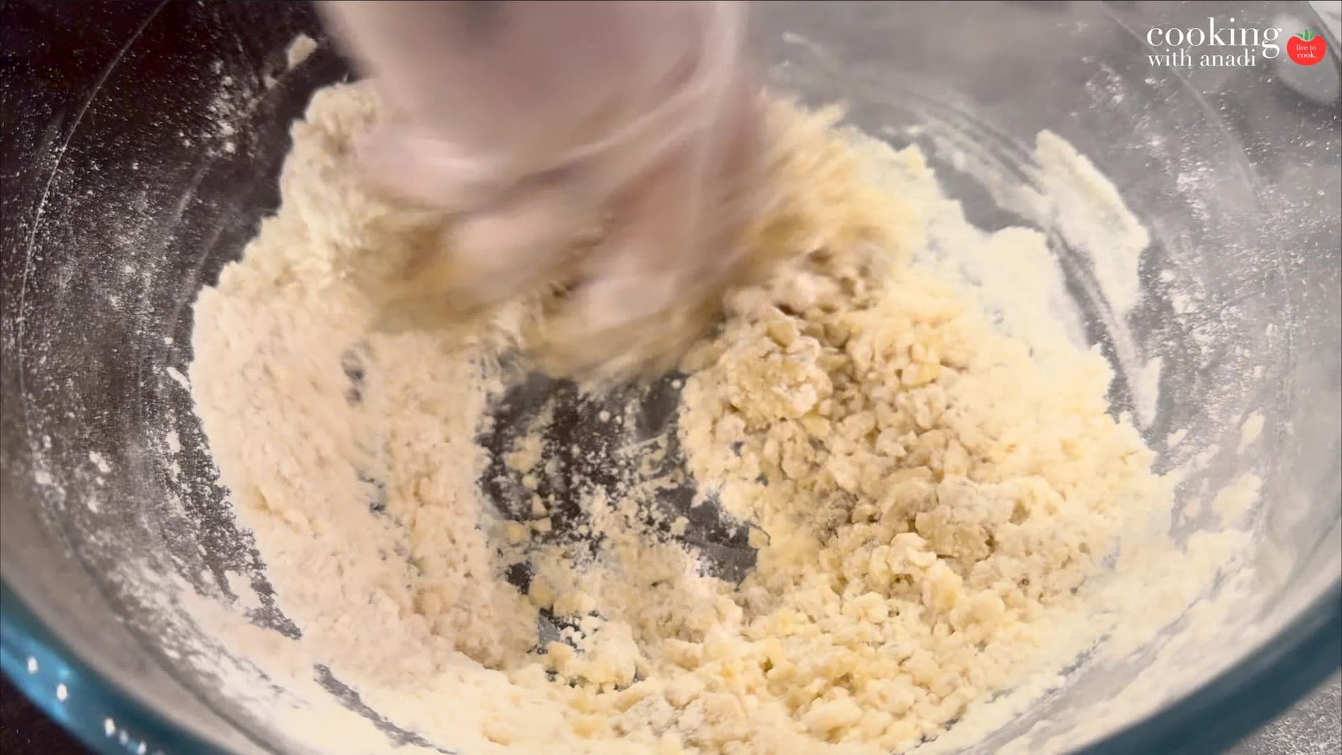 Mixing flour, ajwain, and ghee in a bowl with a hand mixer, showing crumbly dough texture for samosa dough.