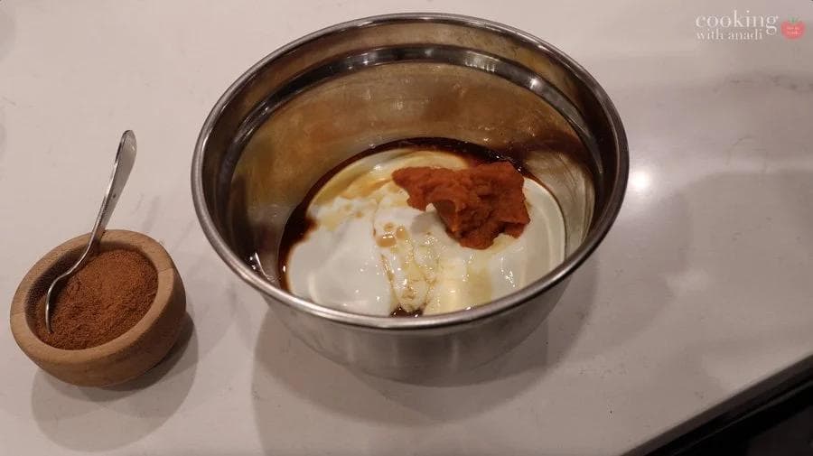 Pumpkin cream cheese filling ingredients in a metal bowl with cinnamon powder sprinkled on top, wooden spoon with cinnamon nearby.