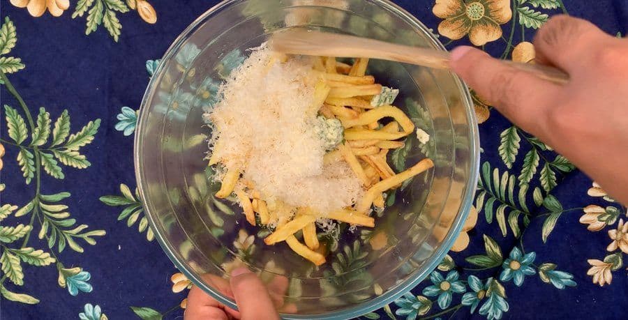 Cooked french fries tossed with grated parmesan cheese and garlic butter in a glass bowl.