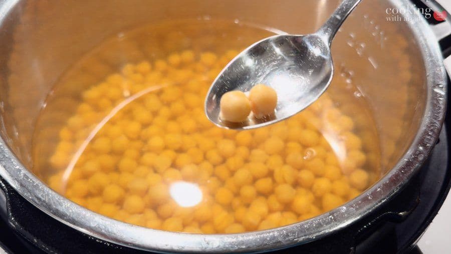 Cooked chickpeas in a pot of liquid being scooped with a spoon for draining.