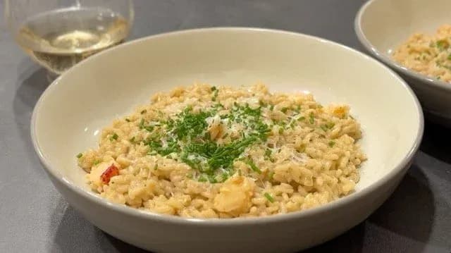 Creamy lobster risotto garnished with fresh parsley and grated cheese in a white bowl with white wine nearby