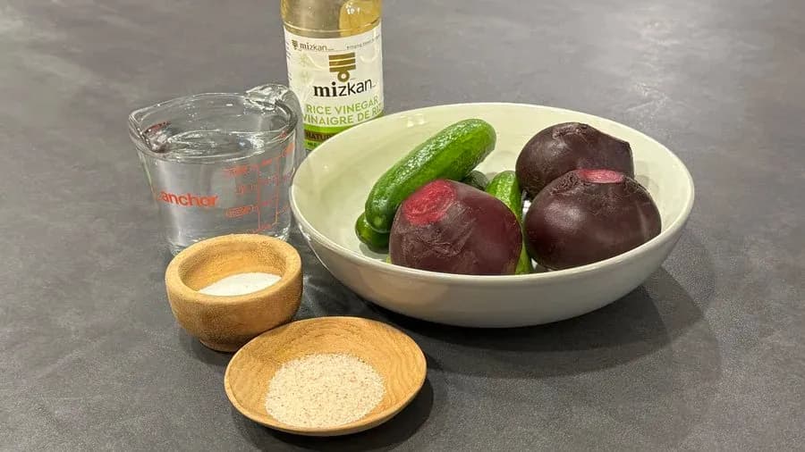 Ingredients for homemade pickled vegetables: cucumbers, beetroot, rice vinegar, salt, sugar, and water in measuring cups and bowl.