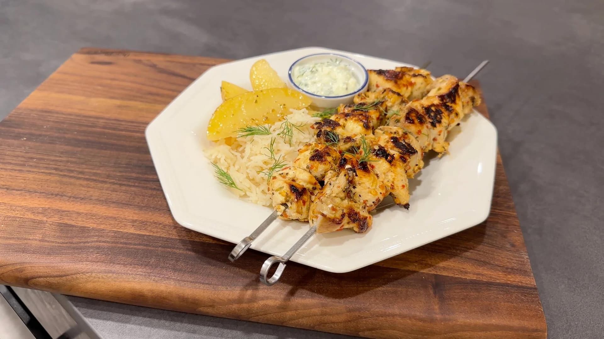 Grilled Greek souvlaki chicken skewers on a white plate with lemon wedges, rice, tzatziki sauce, and fresh dill garnish.
