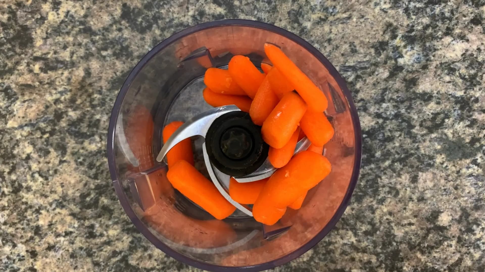 Food processor with blended carrot puree and milk, showing smooth orange mixture with metal blade attachment.