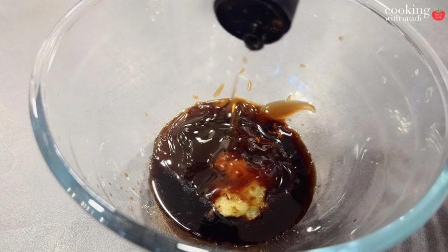 Dark marinade with garlic paste in a glass bowl, with soy sauce being poured in from above.