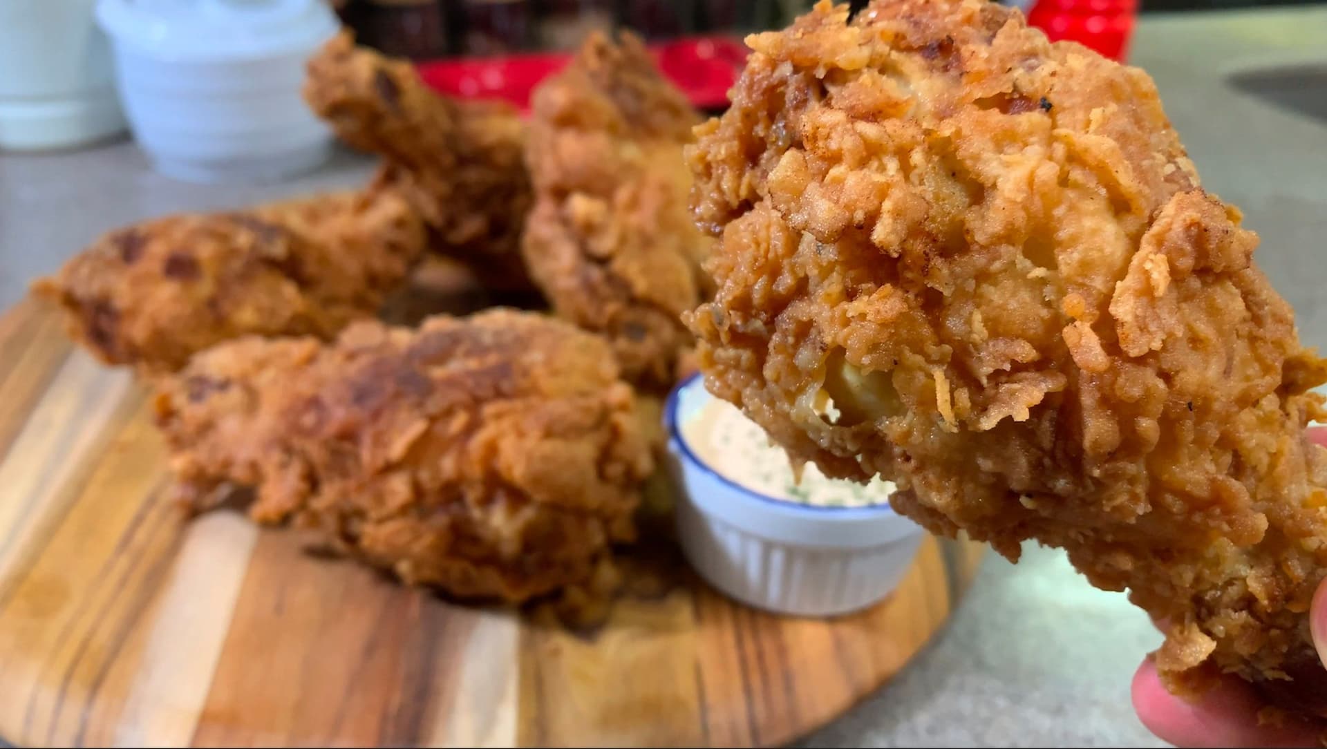 Golden-brown crispy fried chicken pieces on a wooden board with a white dipping sauce container nearby.