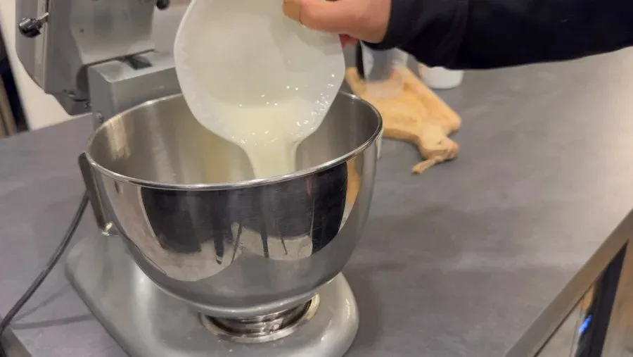 Pouring cream mixture into a stand mixer bowl to prepare gingerbread cold foam.