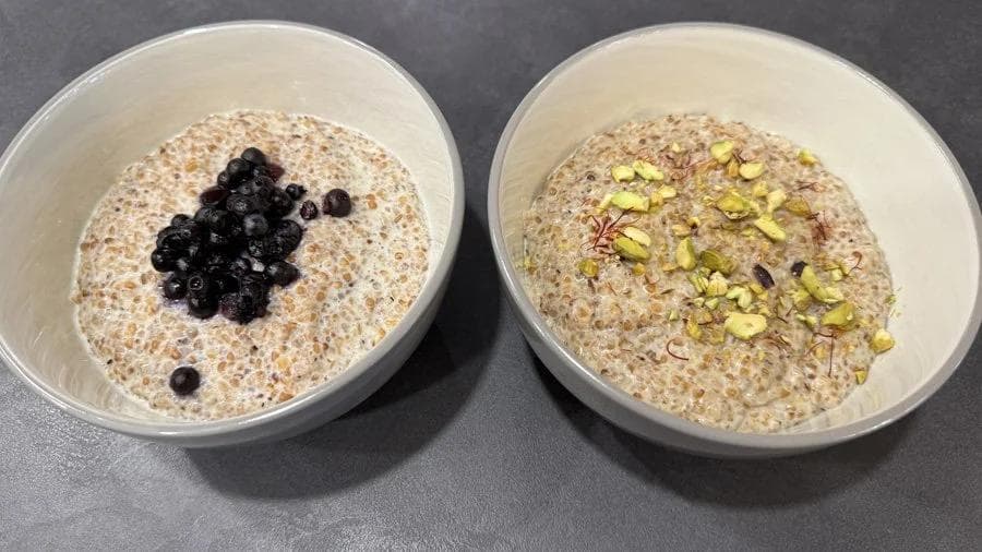 Two bowls of cracked wheat porridge topped with black currants and pistachios.