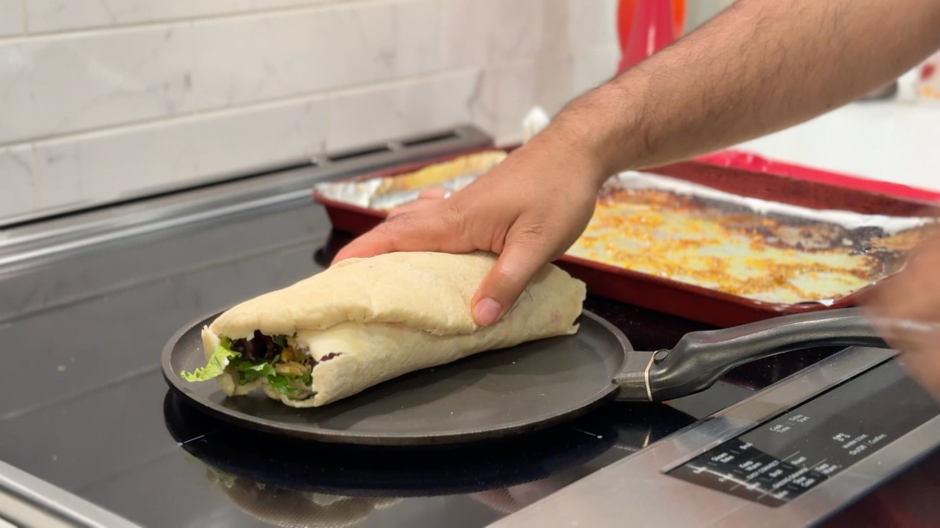 Hand placing a wrapped chicken shawarma sandwich on a dark plate during the browning step.
