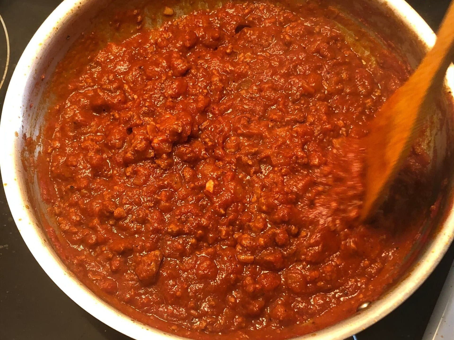 Ground beef and passata sauce simmering in a pot, thickened and releasing oil from the sides.