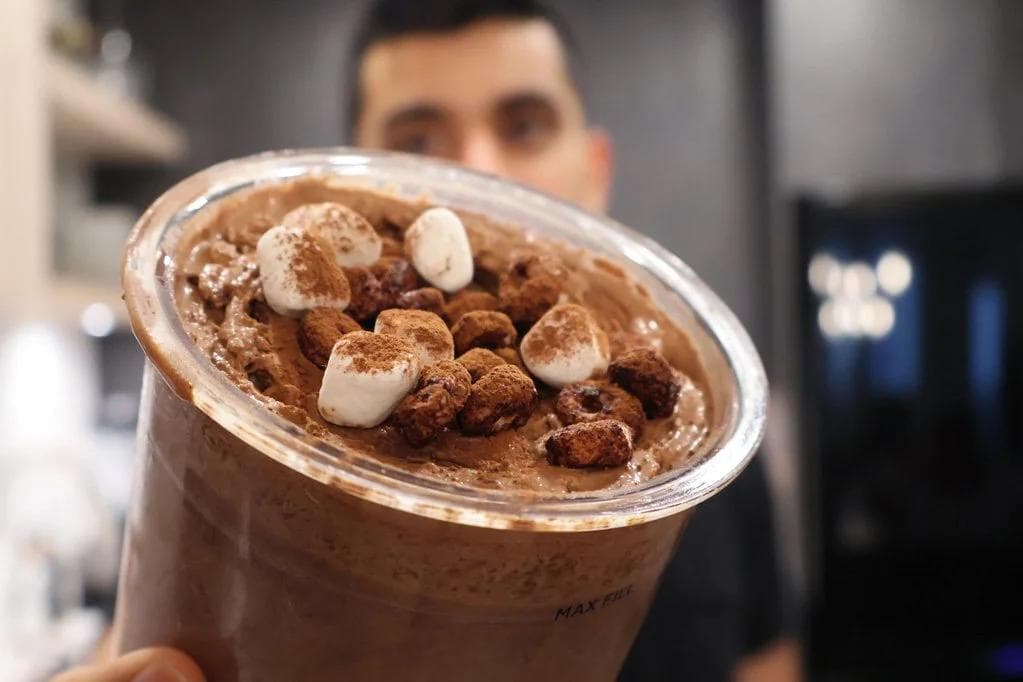 Frozen hot chocolate McFlurry topped with cocoa powder and marshmallows in a clear cup.