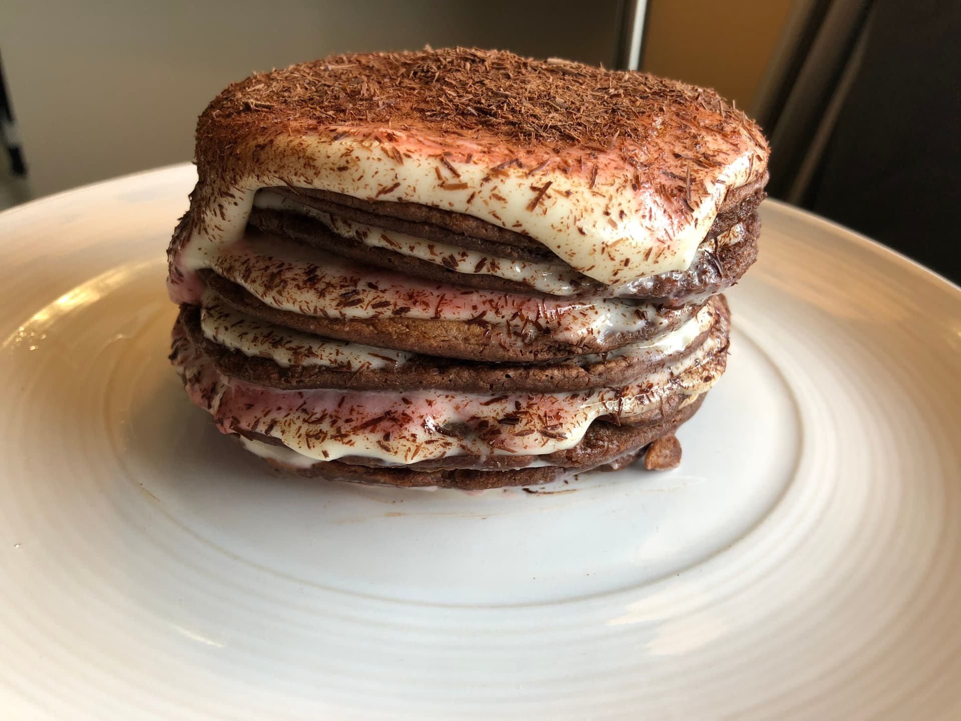 Stack of three chocolate pancakes with cream cheese glaze and cocoa powder dusting on white plate.