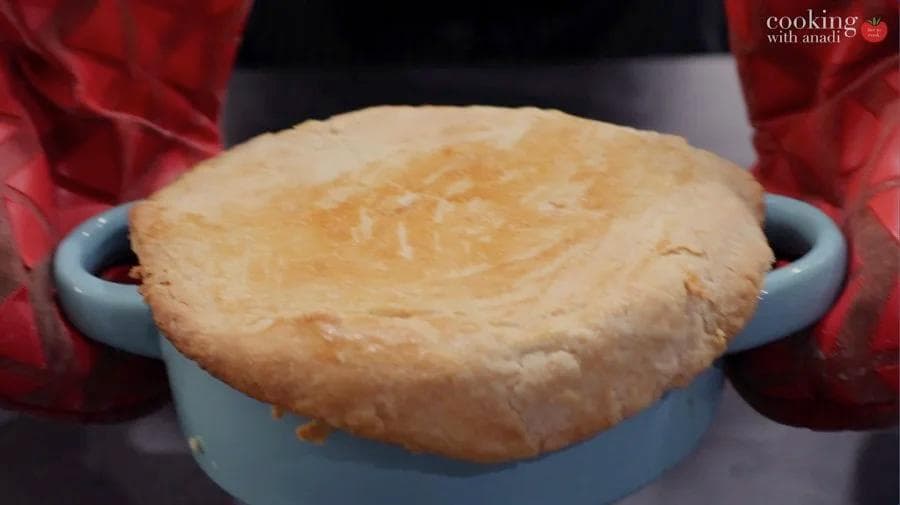 Golden-brown baked chicken pot pie crust in a blue baking dish, held with red oven mitts.