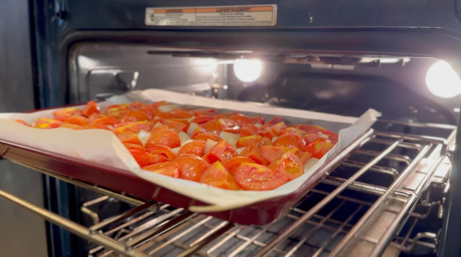 Roasted tomatoes, onions, and garlic on parchment paper in a baking sheet inside an oven.