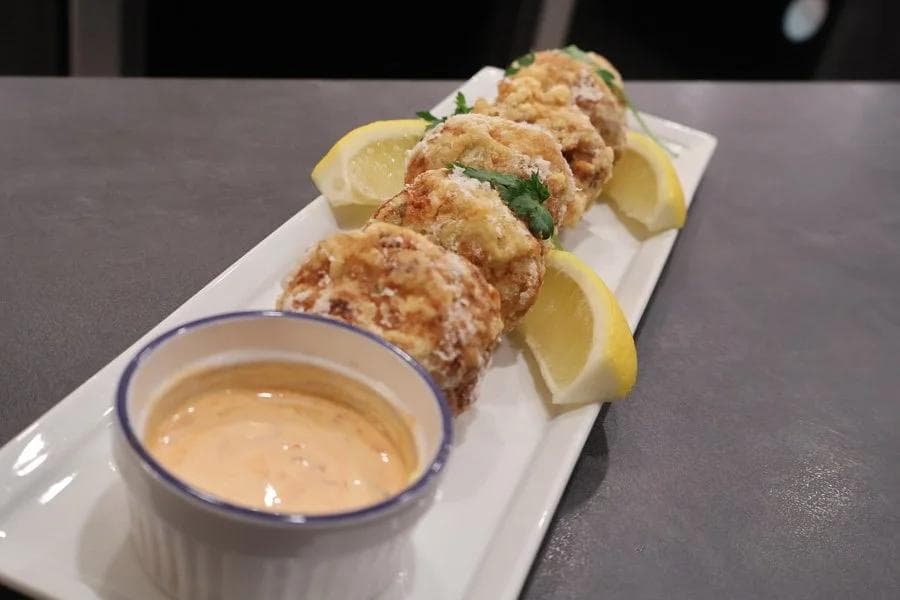 Four golden-brown Indonesian potato fritters on a white plate with lemon wedges and a creamy dipping sauce.