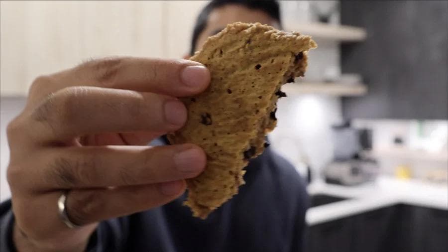 Hand holding a pumpkin protein cookie with chocolate chips, showing its soft, moist texture.