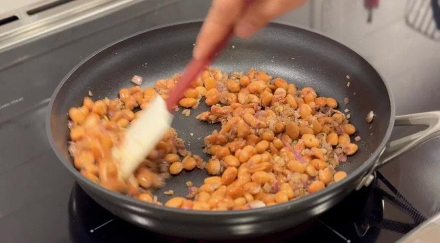 Cooked beans and ground meat being stirred in a skillet with a spatula during sautéing.