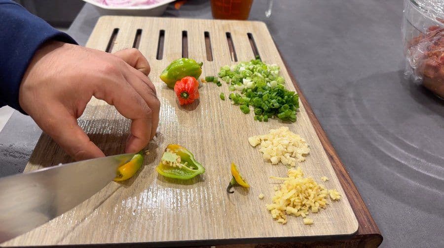 Chef's hands chopping fresh ingredients on wooden board: peppers, garlic, ginger, and green onions for Jamaican pepper steak.