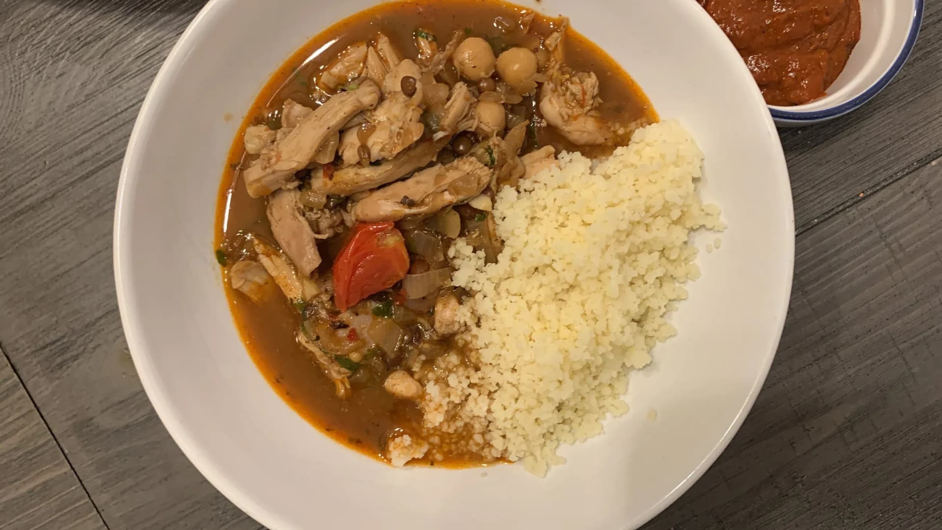 Moroccan chicken and chickpea stew served with fluffy couscous on a white plate, with sauce on the side.