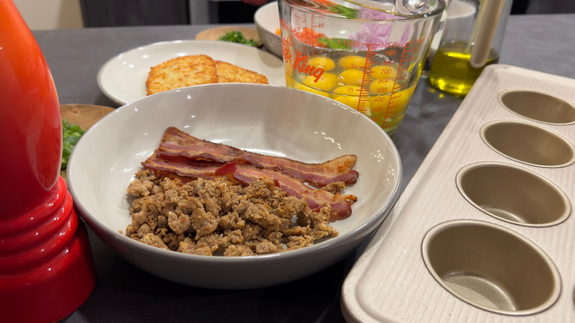 Scrambled eggs with crispy bacon strips in a white bowl, served with crackers and olive oil on the side.