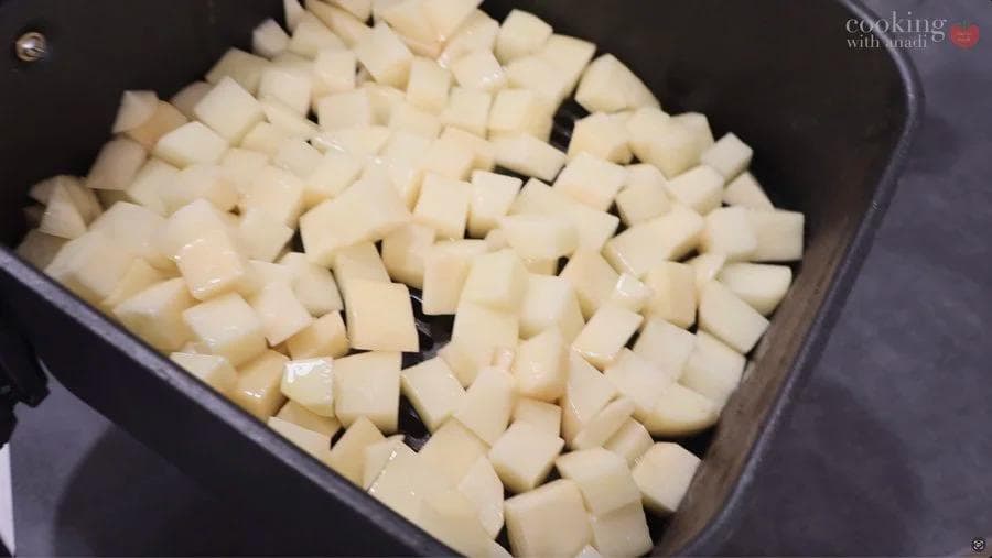 Cubed potatoes coated in olive oil arranged in a single layer in an air fryer basket.