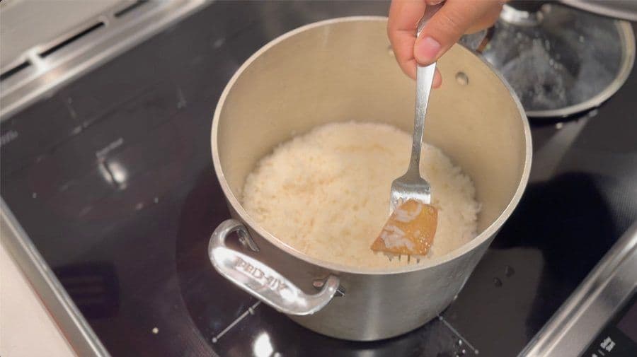 Stirring creamy arroz con leche pudding in a pot with a fork, showing the thick, pale mixture.