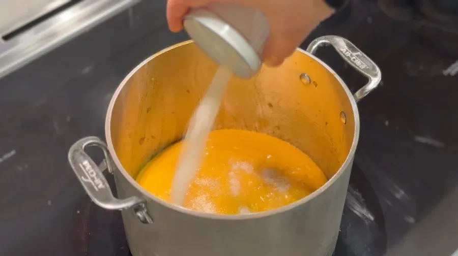 Blending creamy peanut sauce with an immersion blender in a white pot on stovetop.