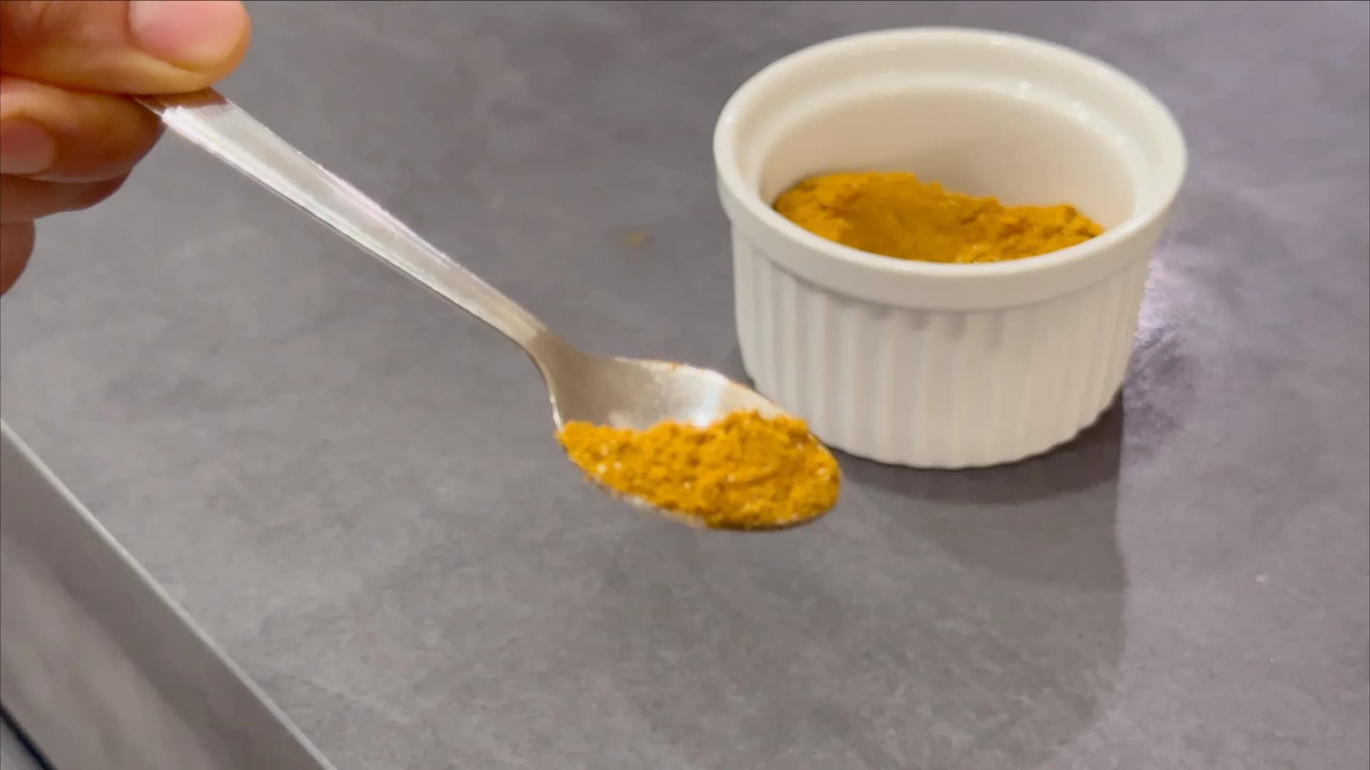 Spoon holding golden curry powder over a white ramekin filled with mixed Nigerian curry spice blend.