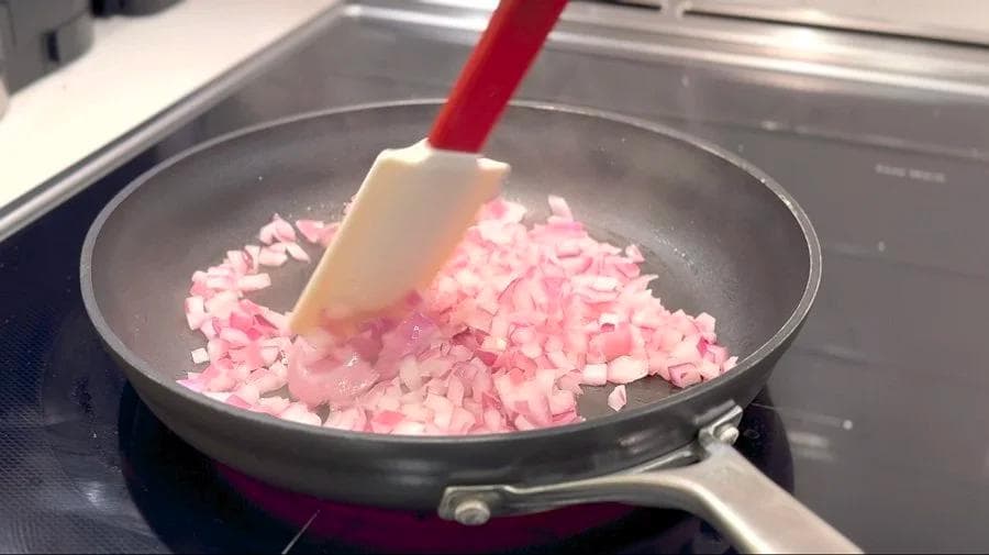 Diced pink onions being stirred in a skillet with a spatula on the stovetop.