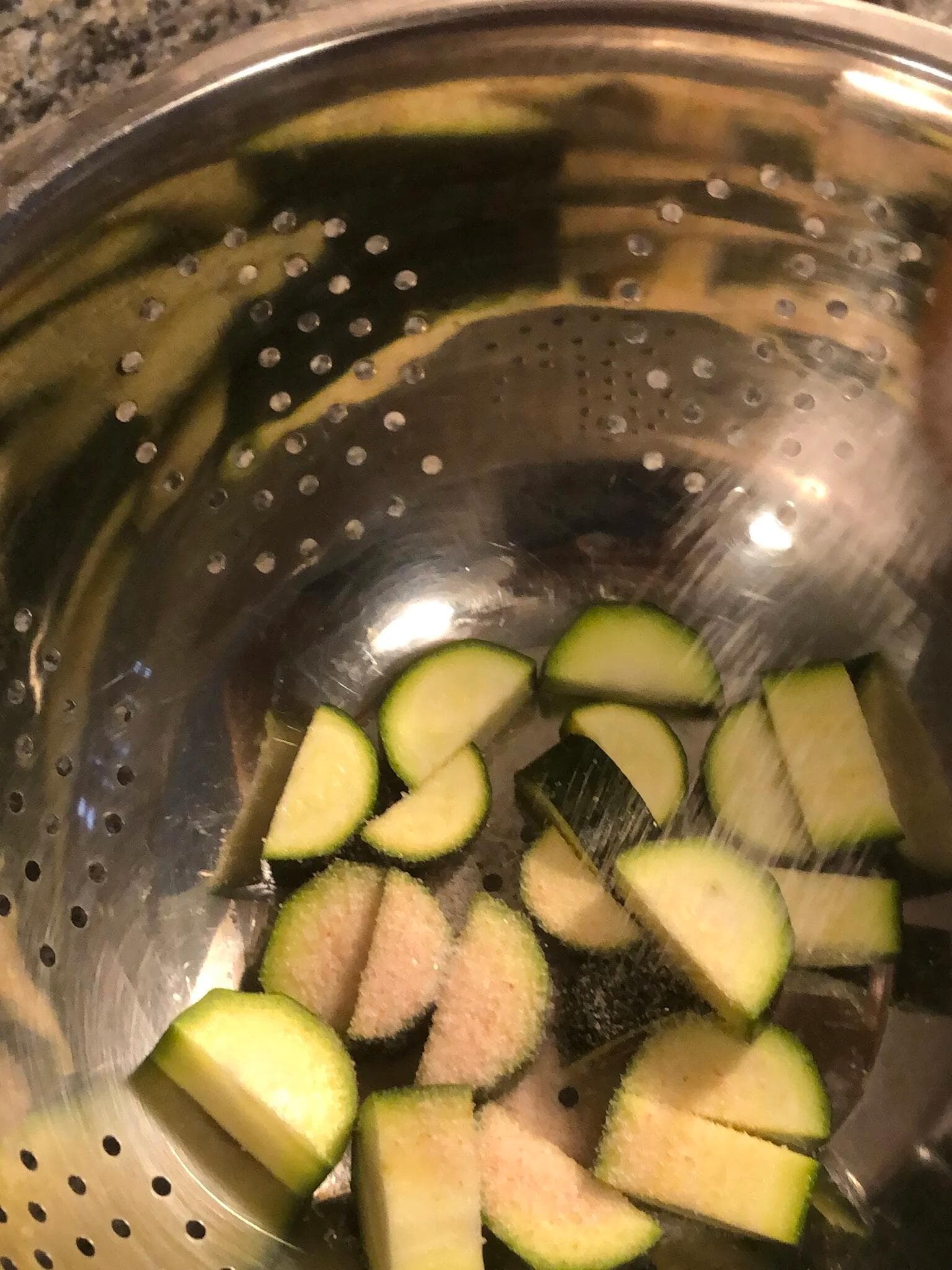 Diced zucchini pieces in a metal colander being salted, draining excess water.