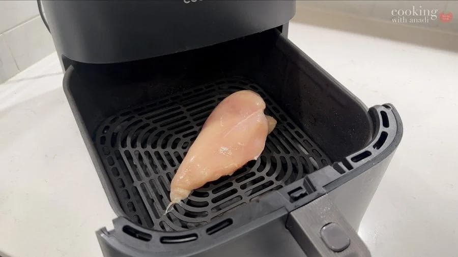 Raw chicken breast placed in air fryer basket, evenly flattened for uniform cooking.